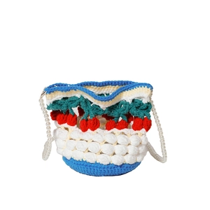 Detailed knit texture of crochet bucket bag with red cherry accents and pearl strap