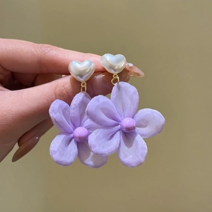 Close-up detail of purple fabric flower earrings with white heart-shaped pearls