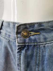 Détail de short en jean taille haute avec bouton en métal bronze et coutures jaunes
