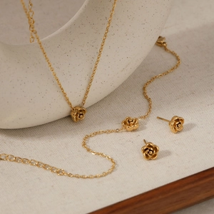 Elegant gold stainless steel camellia necklace and earrings set on beige fabric