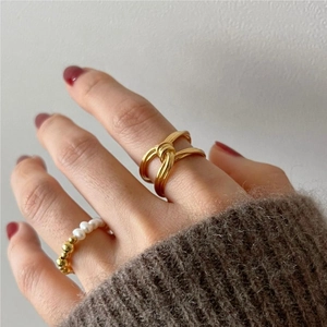 Detailed view of a gold knot ring paired with a dainty pearl band on a hand