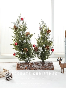 Detail of snowy mini Christmas trees with pine cones and red berries on a rustic wooden base