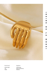 Detailed close-up of golden palm-shaped stainless steel ring on beige satin fabric