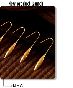 Detailed macro view of high-polished golden water drop earrings on brown textured fabric