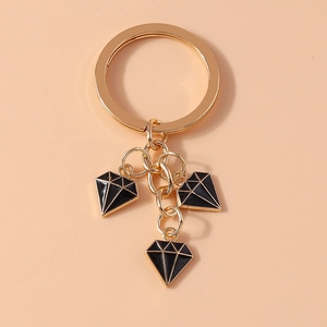Detail of gold keychain with three black enamel diamond-shaped charms on warm orange base