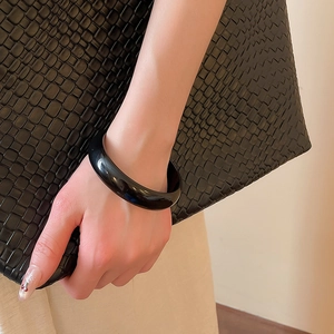 Polished black resin minimalist round bangle worn on wrist with a textured background