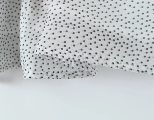 Close-up of white chiffon fabric with black polka dots and high-quality stitching detail