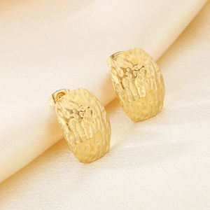 Close-up of golden heart-shaped stud earrings with hammered texture on white silk fabric