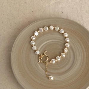 Baroque pearl bracelet with gold T-bar clasp and pendant on a beige ceramic plate
