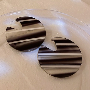 Macro detail of round acrylic earrings with black and white striped geometric design