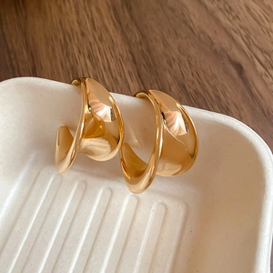 Macro shot of polished gold-toned twisted C-shape metal earrings on a tray
