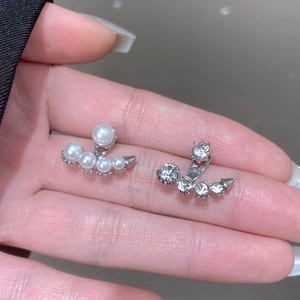 Detalle de pendientes geométricos plateados con circonitas brillantes y perlas blancas