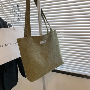 Detail view of green corduroy tote bag with white fashion label hanging on a metal rack