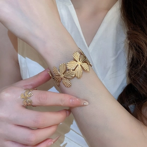 Dettaglio del bracciale rigido dorato e anello coordinato con trama floreale e foglie