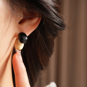 Close-up of a model wearing minimalist black and gold oval geometric drop earrings