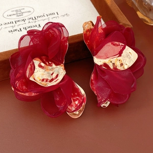 Detail shot of wine red fabric flower earrings with gold center on brown leather
