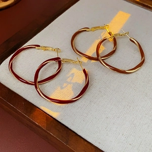 Detail of twisted metal hoop earrings in burgundy and caramel enamel with warm lighting