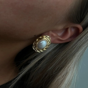 Macro detail of retro golden woven edge earrings with large cream pearls on a model