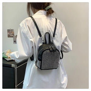 Mini black leather backpack with silver studs shown on a model in white shirt