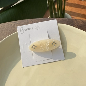 Detail of cream oval acetate hair clip with embossed butterfly and sparkling rhinestones