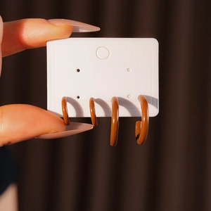 Detailed view of four brown C-shaped resin earrings on a display card held by hand