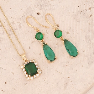 Detail of emerald green zircon pendant necklace and drop earrings on stone background