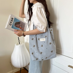 Close-up of light blue corduroy tote bag featuring embroidered bears and heart patterns