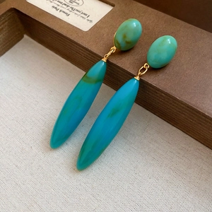 Macro detail of turquoise acrylic drop earrings with gold metal links on a fabric surface