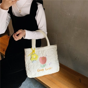 Detail of white quilted tote bag featuring pink tulip embroidery and yellow flower charm