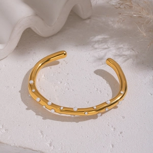 Detail of 18K gold-plated open bangle with white pearls on a minimalist textured surface