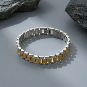 Detail of two-tone gold and silver stainless steel watch strap bracelet on a dark rock