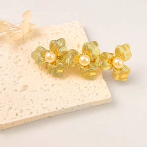 Elegant gold metal hair clip with three flowers and pearls on a beige stone base