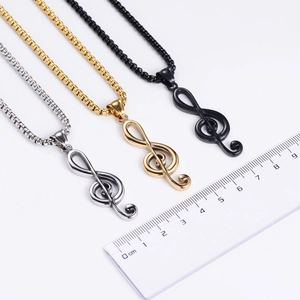 Close-up of G-clef necklaces in silver, gold, and black with a scale ruler for size
