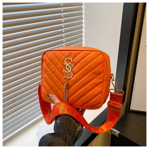 Detail of orange V-quilted camera bag with golden CSC logo and decorative tassel
