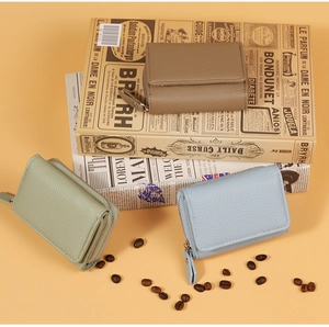 Drei Leder-Mini-Geldbörsen in Braun, Grün und Blau auf einem Vintage-Buch mit Kaffeebohnen