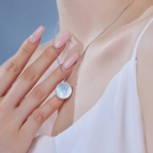 Macro detail of silver necklace featuring round white mother-of-pearl pendant and zircon inlay