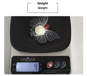 Detail shot of a butterfly wing hair clip with white rose and ladybug on a digital scale