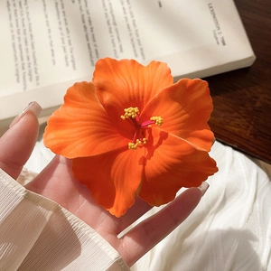 Detail of an orange hibiscus fabric hair clip with realistic textures and yellow stamens