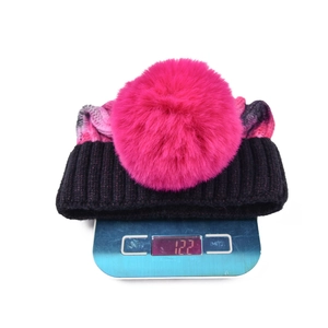 Winter tie-dye knit beanie with pink faux fur pompom shown on scale weighing 122 grams