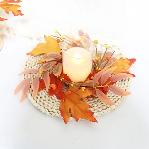 Top view of autumn candle ring with maple leaves, berries, and glass holder on straw mat