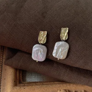 Macro detail of baroque freshwater pearl earrings with gold hammered texture on dark cloth