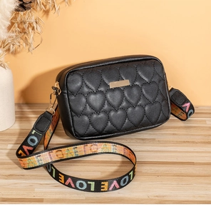 Detail of heart quilted stitching and golden metal plate on black camera crossbody bag