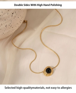 Detail of gold snake chain with black agate pendant on textured fabric background