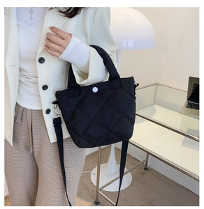 Detail of black quilted nylon bucket bag with round white snap button on a glass desk