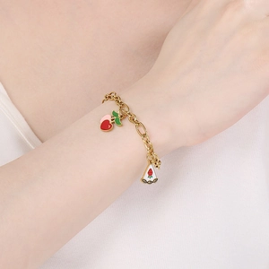 Gros plan du bracelet en acier doré avec des breloques en émail cerise et gâteau aux fraises