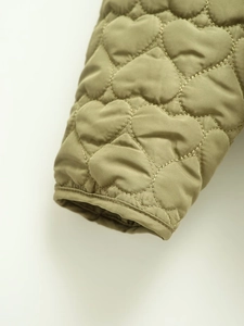Detailed macro view of olive green jacket cuff featuring unique heart-shaped quilting patterns