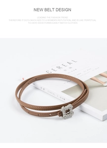 Detail view of a slim brown leather belt for women with a square rhinestone buckle on a magazine