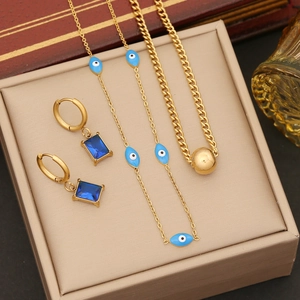 Layered gold evil eye necklace and emerald drop earrings displayed on a gift box