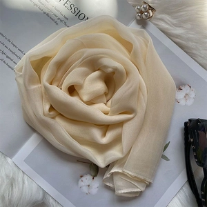 Elegant cream silk scarf shaped like a rose on a magazine with pearl ring and sunglasses