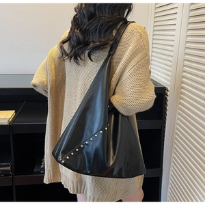 Detail of a large black tote bag with metal rivet studs worn by a model in a knit sweater
